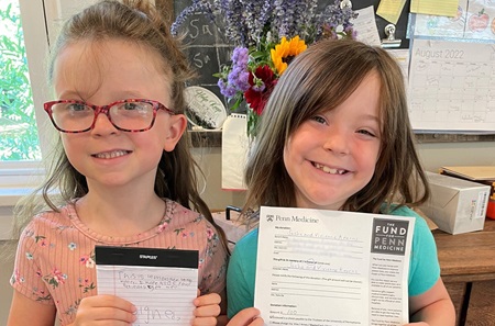 Twin sisters Sasha and Vivienne holding a handwritten letter and donation form for Pennsylvania Hospital